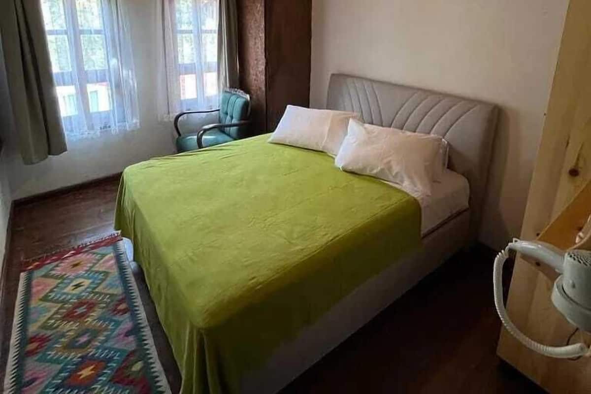 A bedroom with a bed, a chair, a window with curtains, and a wooden ceiling.