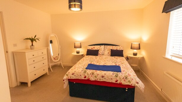 Ein Schlafzimmer mit Bett, Nachttischlampen, einem Schminktisch, einem Spiegel und einer Zimmerpflanze.