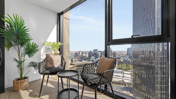 A modern balcony with two chairs and a small table, large windows offering a city view, and potted plants. - Heart of Southbank, Walk to Crown, Resort style amenities & Free Carpark (Southbank)