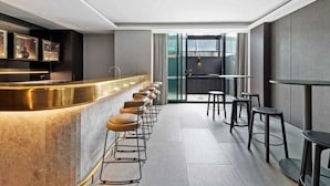 A modern bar area with a long counter and multiple stools, a kitchen visible through a glass partition, and a seating area with tables and chairs. - Heart of Southbank, Walk to Crown, Resort style amenities & Free Carpark (Southbank)