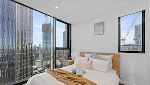 A bedroom with a large bed, a wooden headboard, and a view of a cityscape through floor-to-ceiling windows. - Heart of Southbank, Walk to Crown, Resort style amenities & Free Carpark (Southbank)