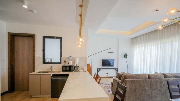 A modern kitchen with a central island, a dining area with a sofa, and a living room with a TV. - Riverbank 1-bedroom apartment in terrific Nairobi Pool & Gym (Nairobi)