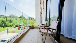 A balcony with a glass railing, a wooden floor, and a view of a playground. - Riverbank 1-bedroom apartment in terrific Nairobi Pool & Gym (Nairobi)