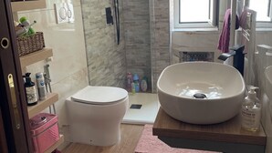 A modern bathroom with a glass-enclosed shower, a freestanding toilet, and a large sink with a marble basin.