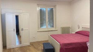 A bedroom with a bed, a window, a radiator, and a wardrobe.