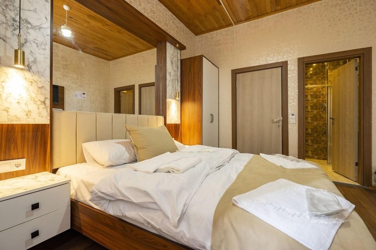 A hotel room with a wooden ceiling, a marble wall, a bed with white linens, a nightstand, and a wardrobe.