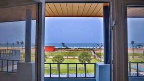 Uitzicht vanaf een balkon op een strand met een houten terras, palmbomen en een heldere lucht.