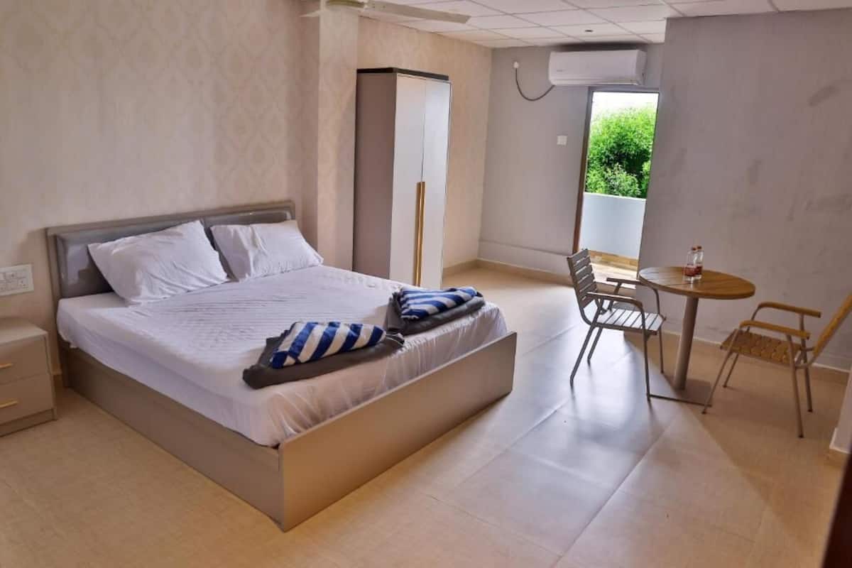A bedroom with a bed, a wardrobe, a table with chairs, and a window with a view.