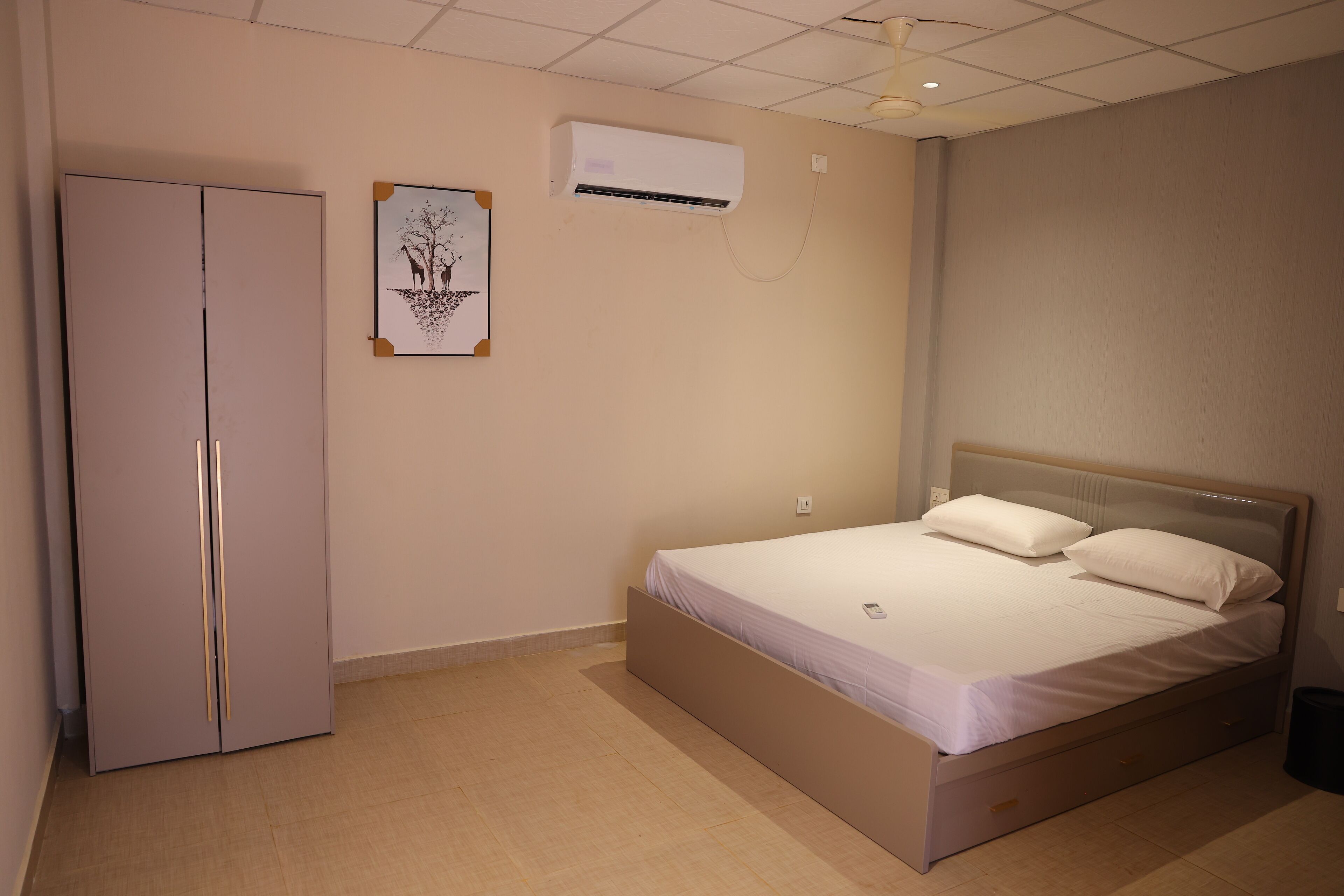 A bedroom with a bed, a wardrobe, an air conditioning unit, and a wall-mounted picture.
