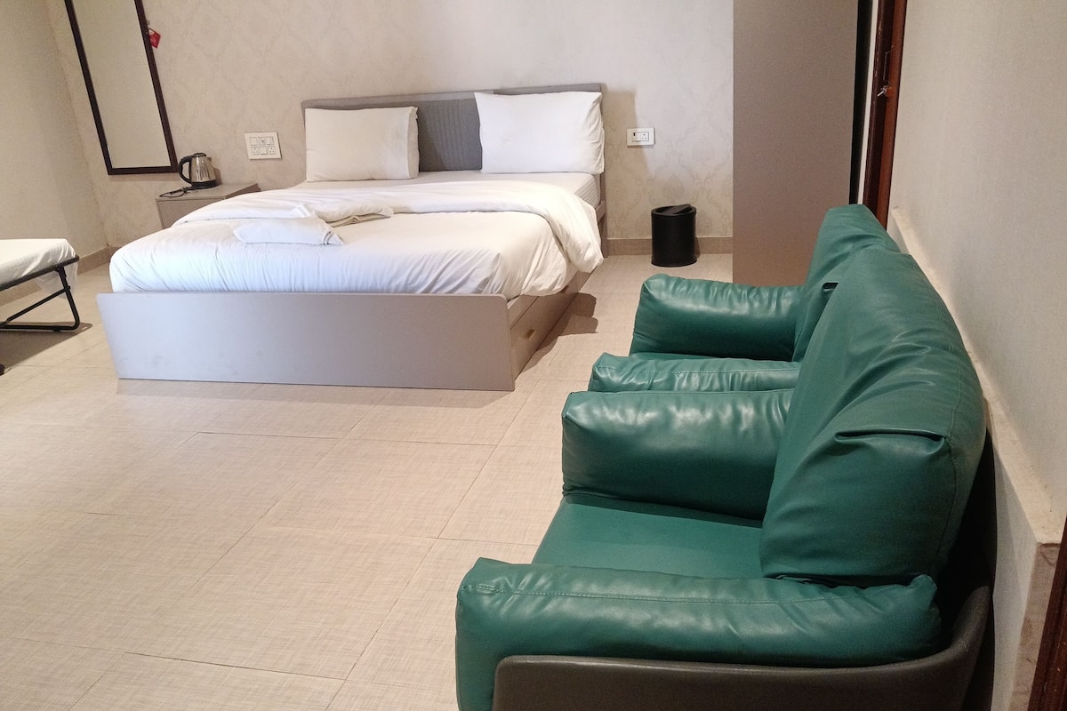 A room with a bed, a green leather sofa, a small table, and a trash bin.