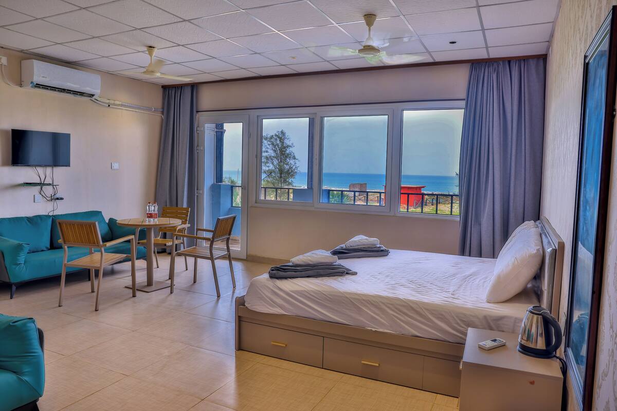 A hotel room with a bed, a desk, a chair, a sofa, and a view of the sea.