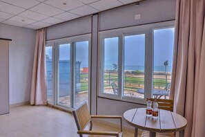 A room with large windows, a round table with chairs, and a view of a beach and park. - THARANG RESORTS APTDC (Ramathirtham)