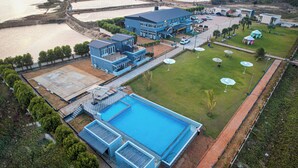 Luchtbeeld van een hotel met een groot zwembad, meerdere gebouwen en een aangelegde tuin met parasols.