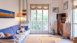 A living room with a blue sofa, a wooden cabinet, a television, and a large window with curtains. - Stylish flat balcony near Rapallo Castle (Rapallo)