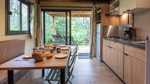 Een moderne keuken met houten kastjes, een ontbijt gedekte eettafel, en uitzicht op het bos door de glazen deur.