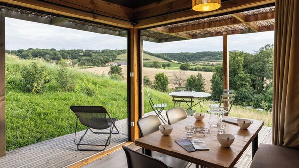 Een houten eetgedeelte met een tafel gedekt voor vier personen, met uitzicht op een weelderig groen landschap.