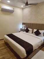 A hotel room with a large bed, a ceiling fan, an air conditioner, and a textured wall.