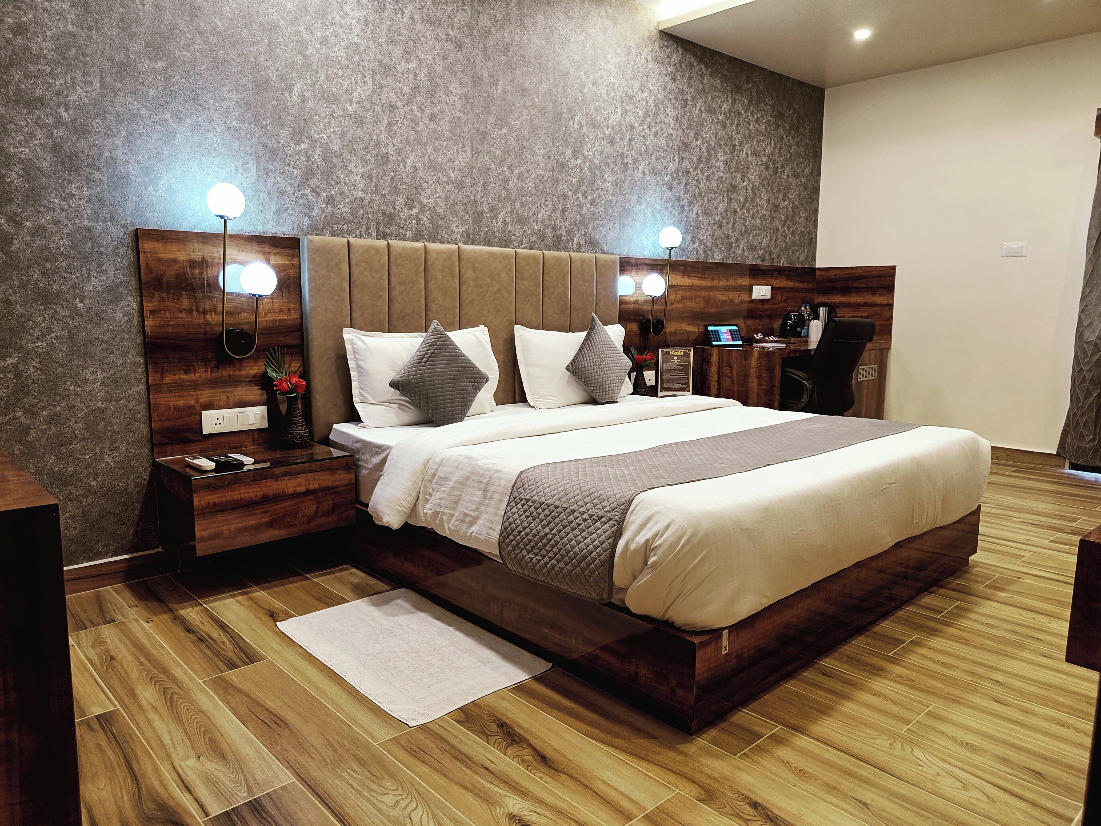 Un dormitorio moderno con una cama grande, cabecera de madera, lámparas de noche, una mesita de noche y un escritorio con una computadora portátil.
