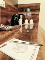 A wooden table with a coffee maker, cups, and a notebook.