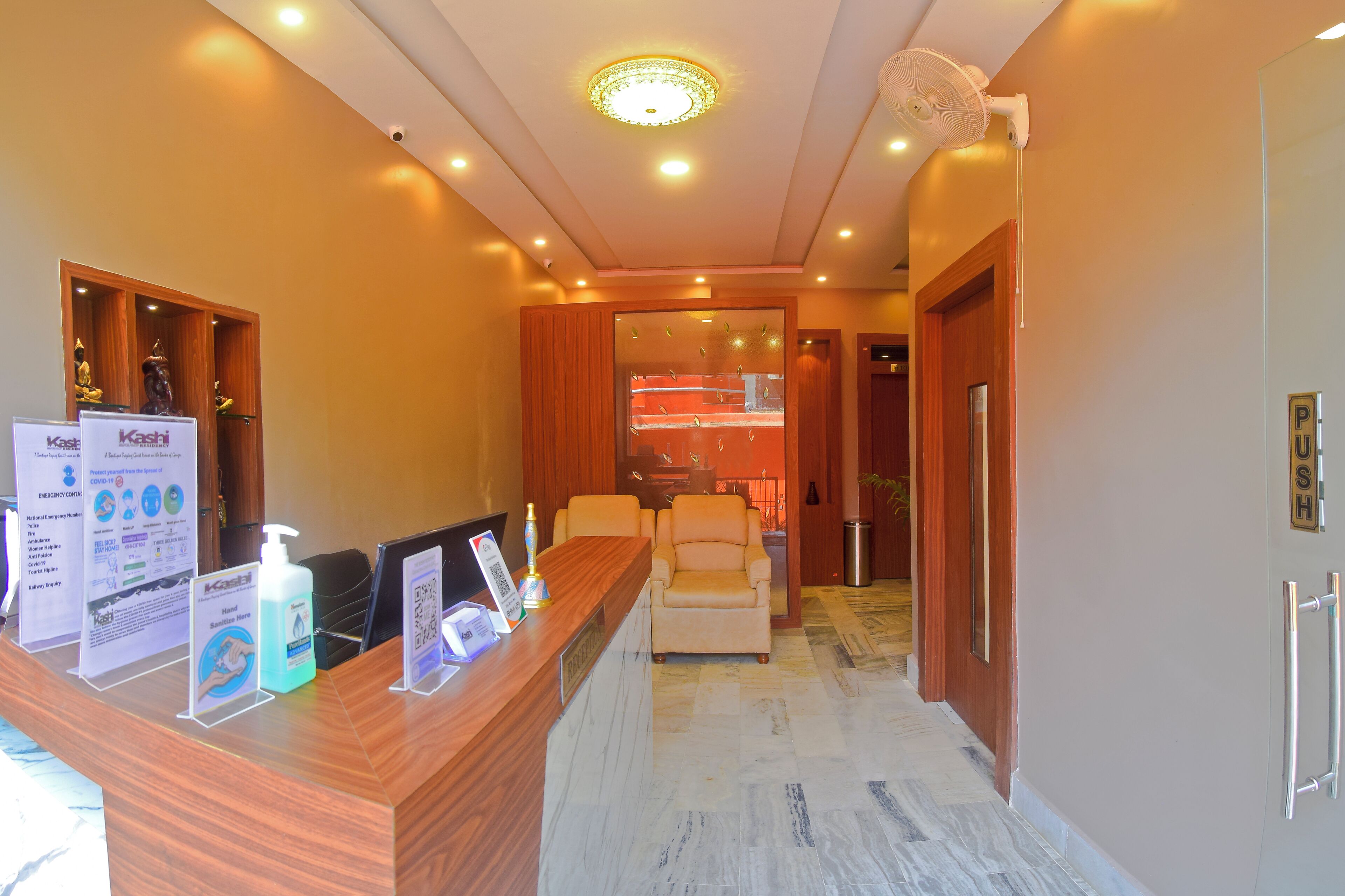 Zona de recepción con mostrador de madera, área de asientos con sillas y vista a una habitación con cama y ventana.