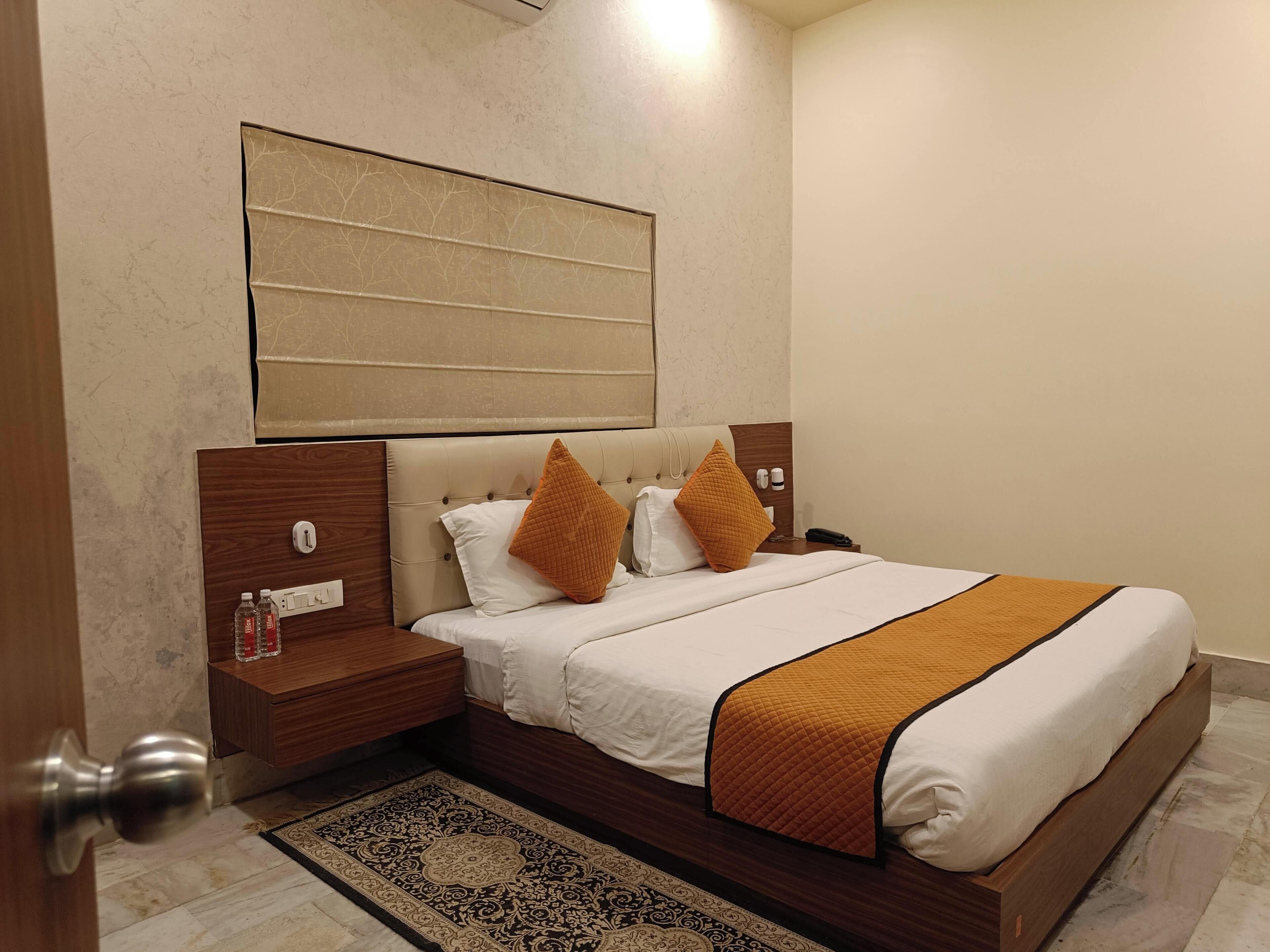 A hotel room with a large bed, two nightstands, a wooden headboard, a patterned rug, and a wall-mounted artwork.