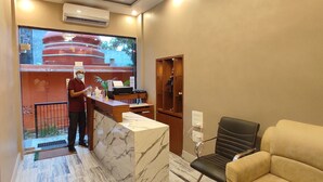 A reception area with a marble reception desk, a black leather chair, and a wooden cabinet with a decorative item. - THE KASHI RESIDENCY  (Varanasi)
