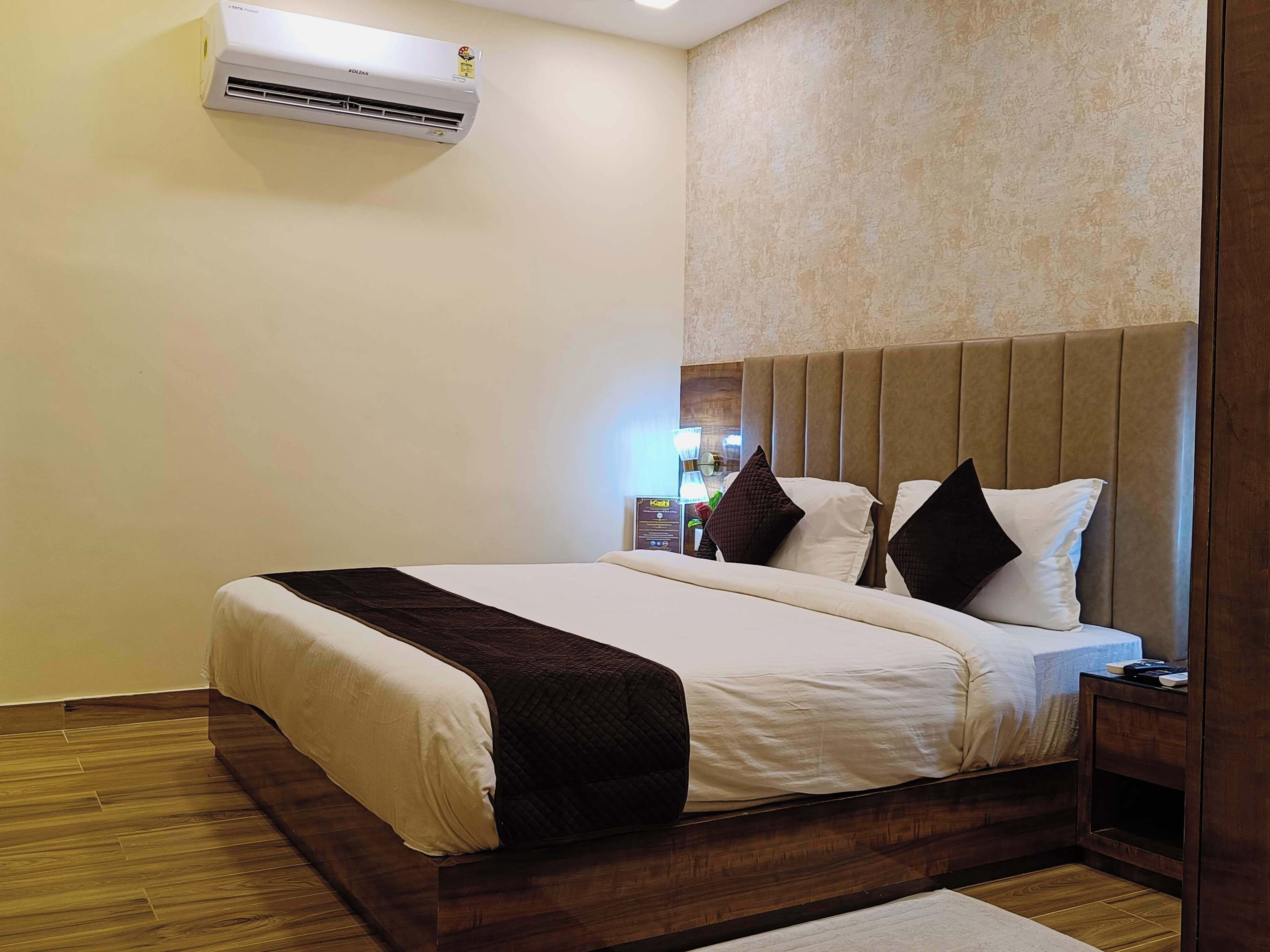 A hotel room with a bed, a nightstand, a wall-mounted air conditioner, and a textured wall.