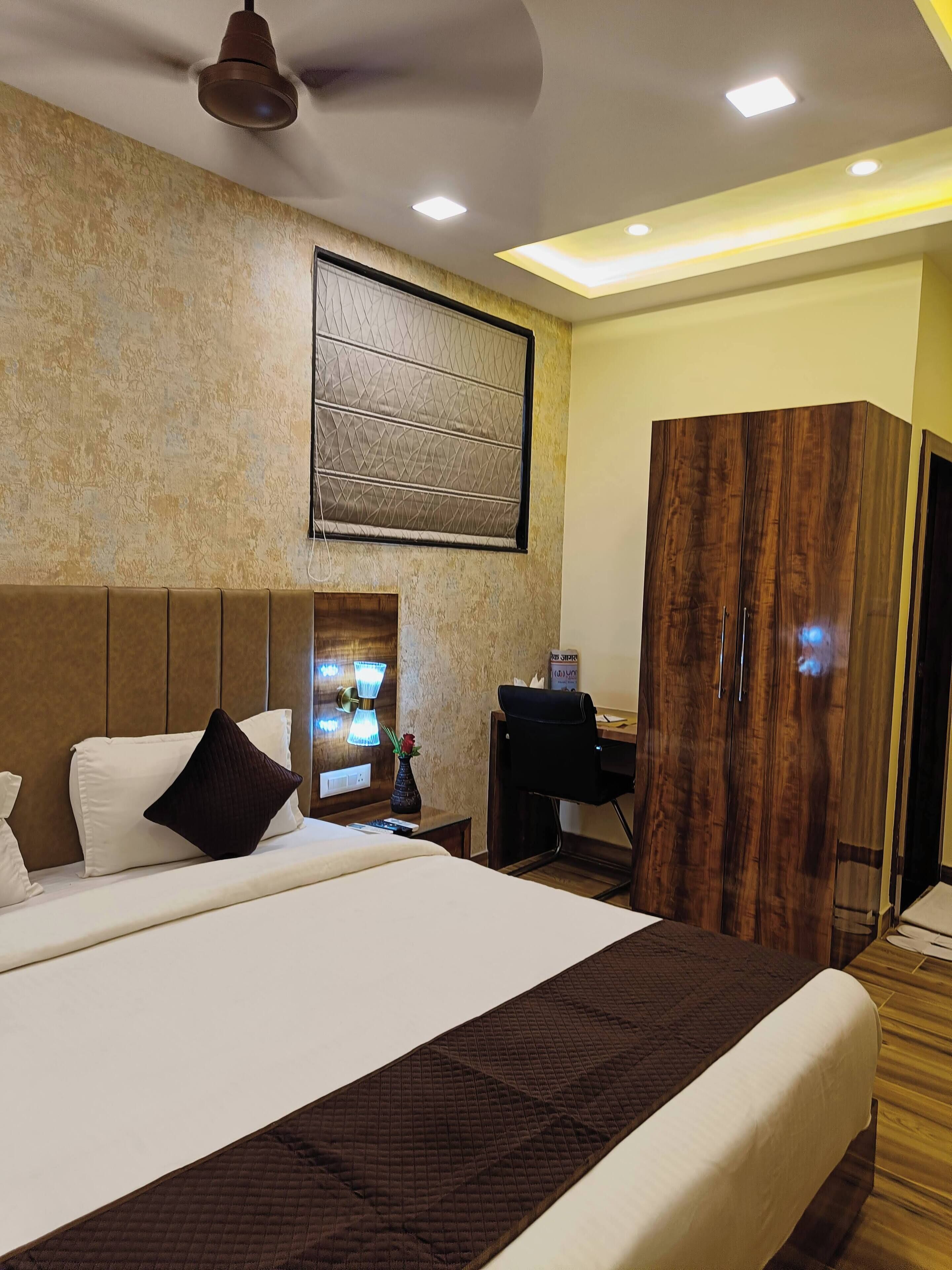 A hotel room with a large bed, a wooden wardrobe, a desk, and a wall-mounted TV.