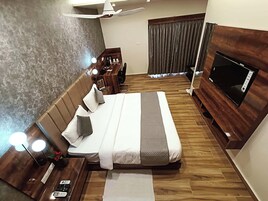 A hotel room with a large bed, bedside tables, a desk, a chair, a TV, and a ceiling fan.