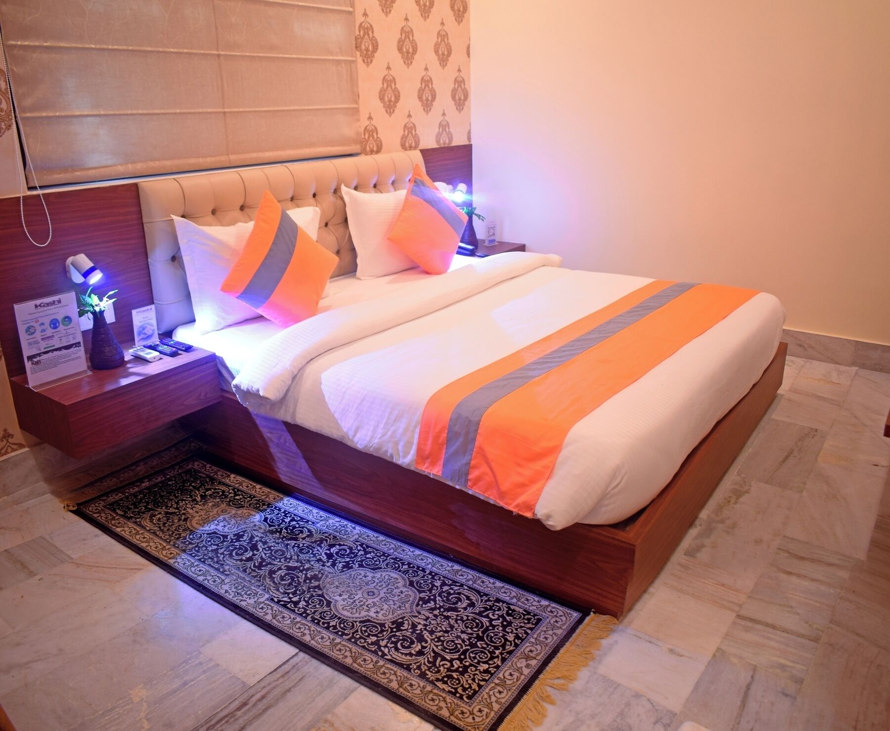 A neatly made bed with a striped bedspread, a nightstand with a lamp, and a patterned rug.