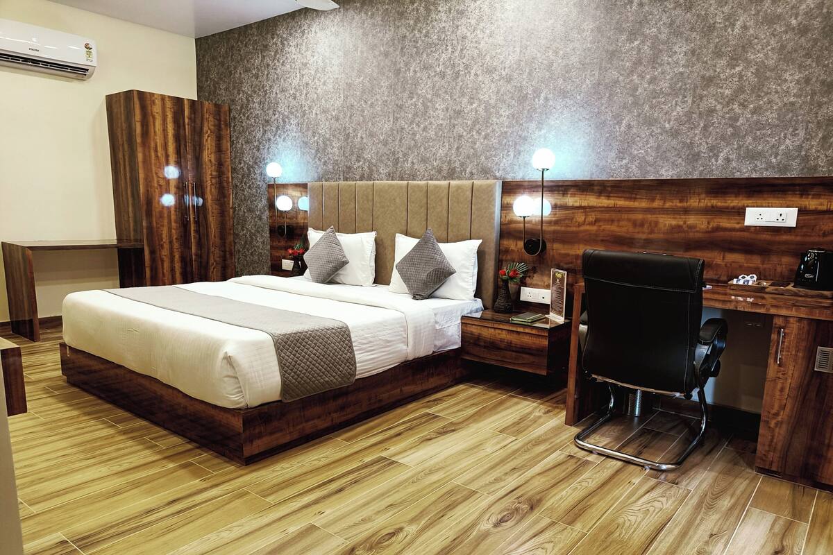 Habitación de hotel con una cama grande, cabecero de madera, mesitas de noche con lámparas, un escritorio con una silla y un armario empotrado.