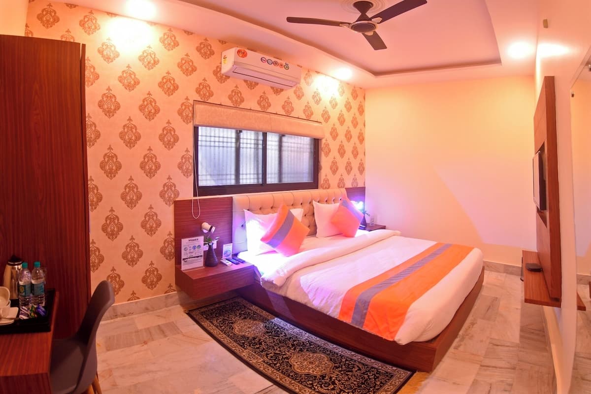 Habitación de hotel con cama, escritorio, silla, ventilador de techo y aire acondicionado.