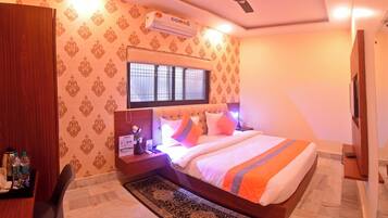 A hotel room with a bed, a desk, a chair, a ceiling fan, and an air conditioning unit.