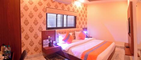 Habitación de hotel con cama, escritorio, silla, ventilador de techo y aire acondicionado.