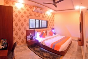 A hotel room with a bed, a desk, a chair, a ceiling fan, and an air conditioning unit.