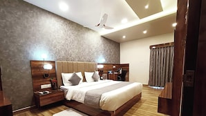 A modern hotel room with a large bed, wooden headboard, bedside tables, a desk, and a ceiling fan. - THE KASHI RESIDENCY  (Varanasi)