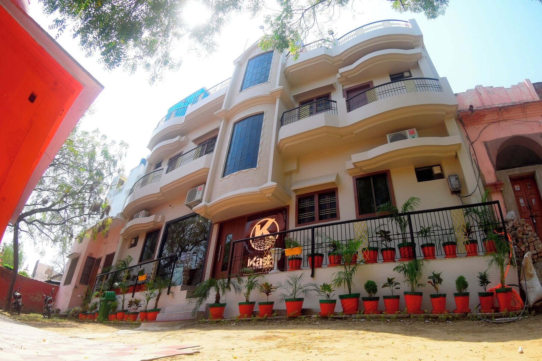 Un edificio de varios pisos con balcones, entrada protegida por una reja y plantas en macetas a lo largo de la fachada.