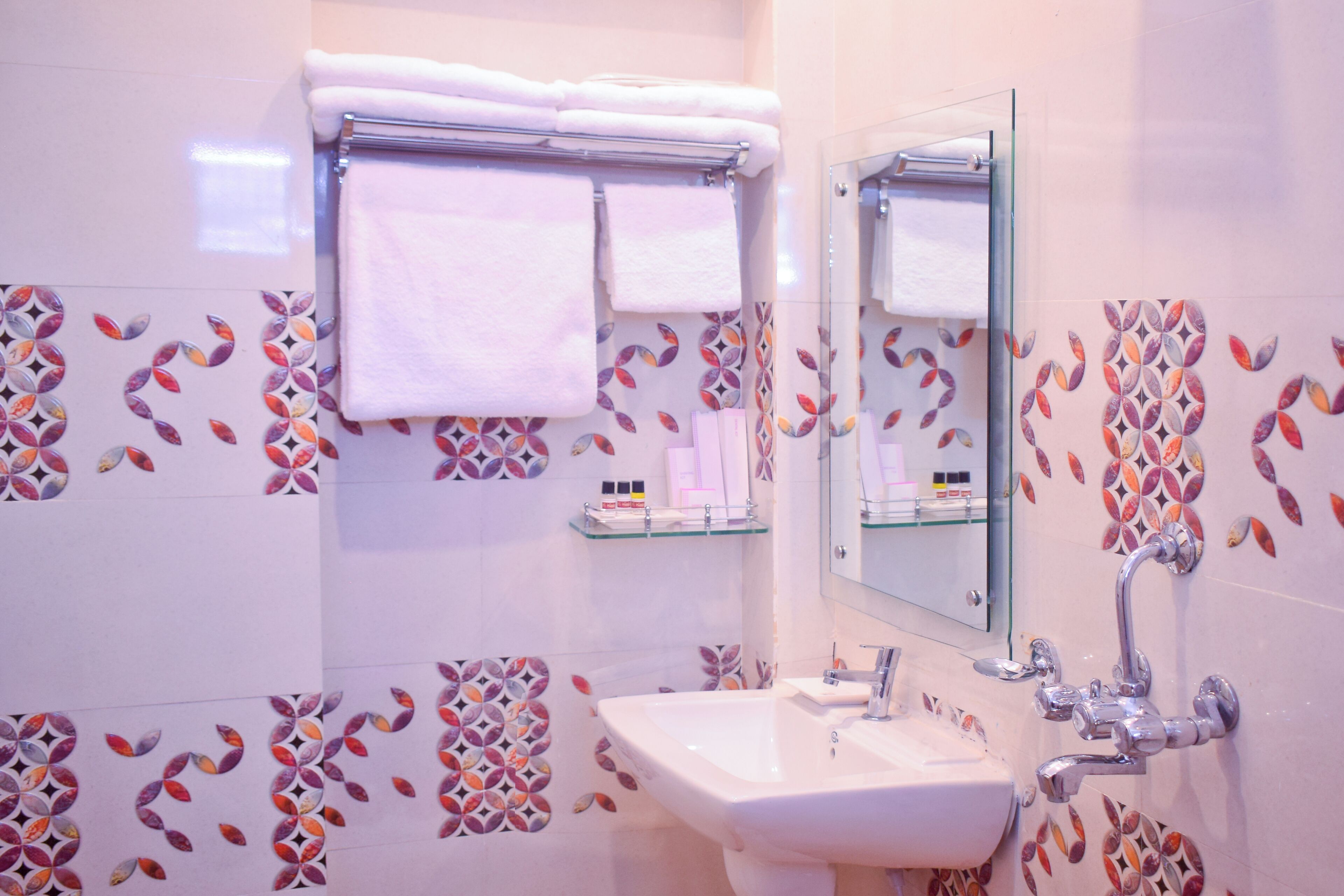 Ett badrum med en vit tvättställ, en glashylla och en handdukshängare med två handdukar.
