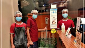 Three individuals standing at a counter with a sign indicating COVID-19 prevention measures. - THE KASHI RESIDENCY  (Varanasi)