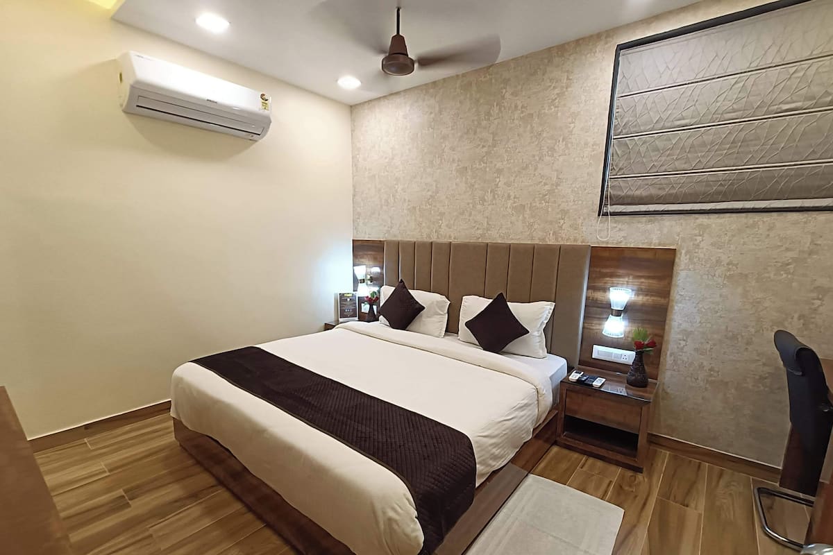 Habitación de hotel con una cama grande, una mesita de noche con lámpara, aire acondicionado y ventilador de techo.