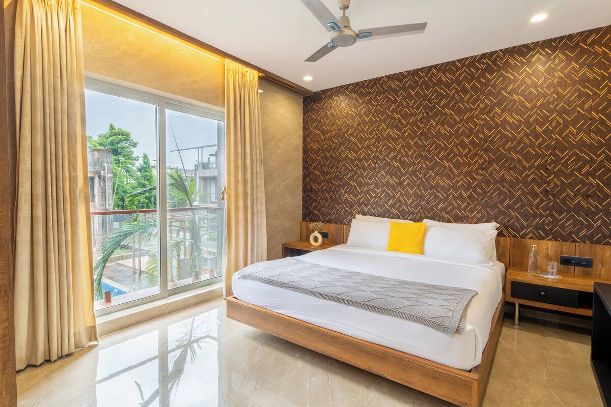 A modern hotel room with a large bed, a ceiling fan, a wooden headboard, and a view of the outside.