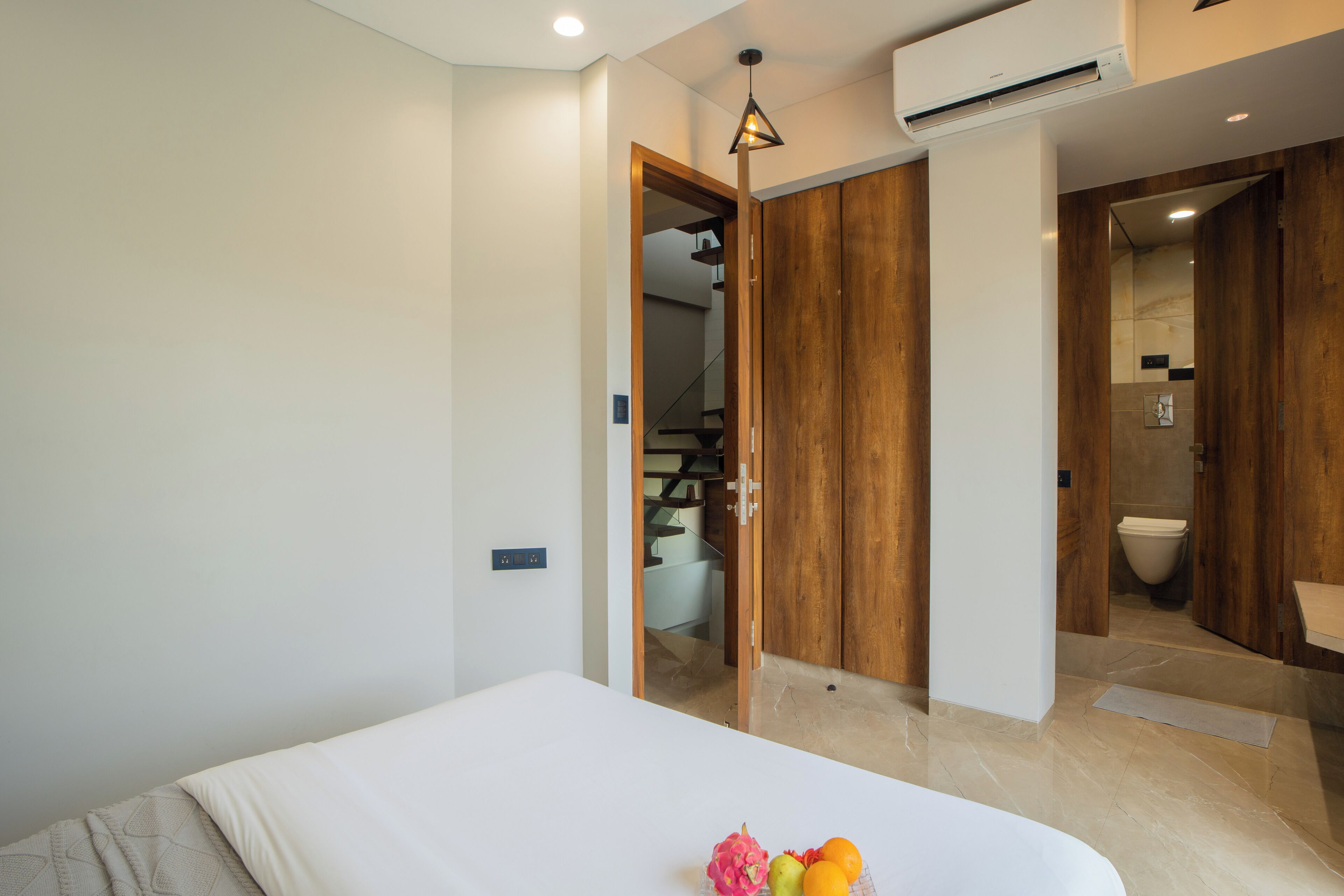 A modern bedroom with a bed, a wooden wardrobe, and a bathroom visible through an open door.