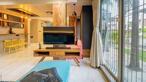 Una sala de estar moderna con un televisor grande, detalles de madera y vistas a través de un ventanal.