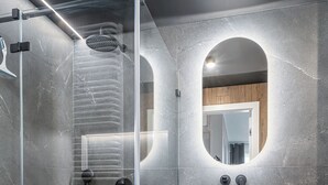 Ett modernt badrum med en duschavdelning med glasväggar, ett badrumsskåp i trä och en stor spegel.
