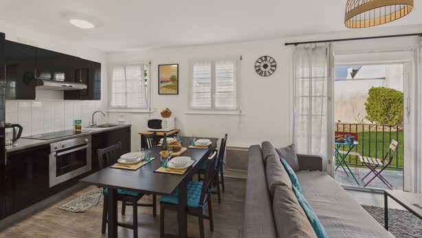 Une cuisine moderne avec des meubles de couleur sombre, un coin repas doté d’une longue table et un espace salon confortable avec un canapé et des fauteuils.