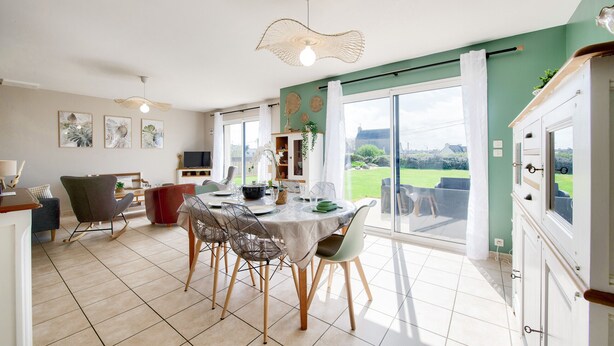 Un espace repas avec une table ronde, des chaises et une vue dégagée grâce à de grandes fenêtres.