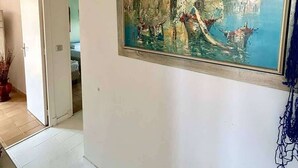 Une pièce avec un grand tableau représentant un paysage côtier, des murs blancs et un sol carrelé.