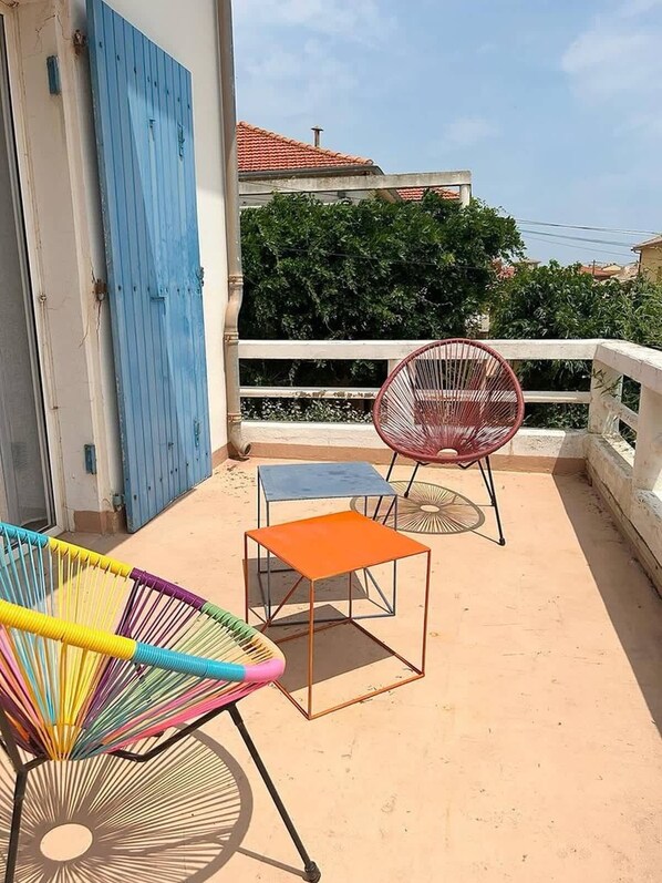 A balcony with a blue door, a white railing, and a view of a house with a red roof. - ValrasLoc Seaside Apartment (Valras-Plage)