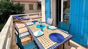 Un balcon avec une table dressée pour le dîner, des volets bleus et une vue sur les environs.