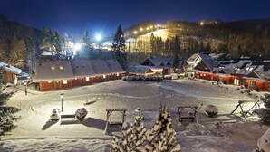 A snow-covered courtyard with wooden cabins, a central gathering area, and a mountain backdrop. - Dolina Leśnicy SKI & SPA Resort (Brenna)